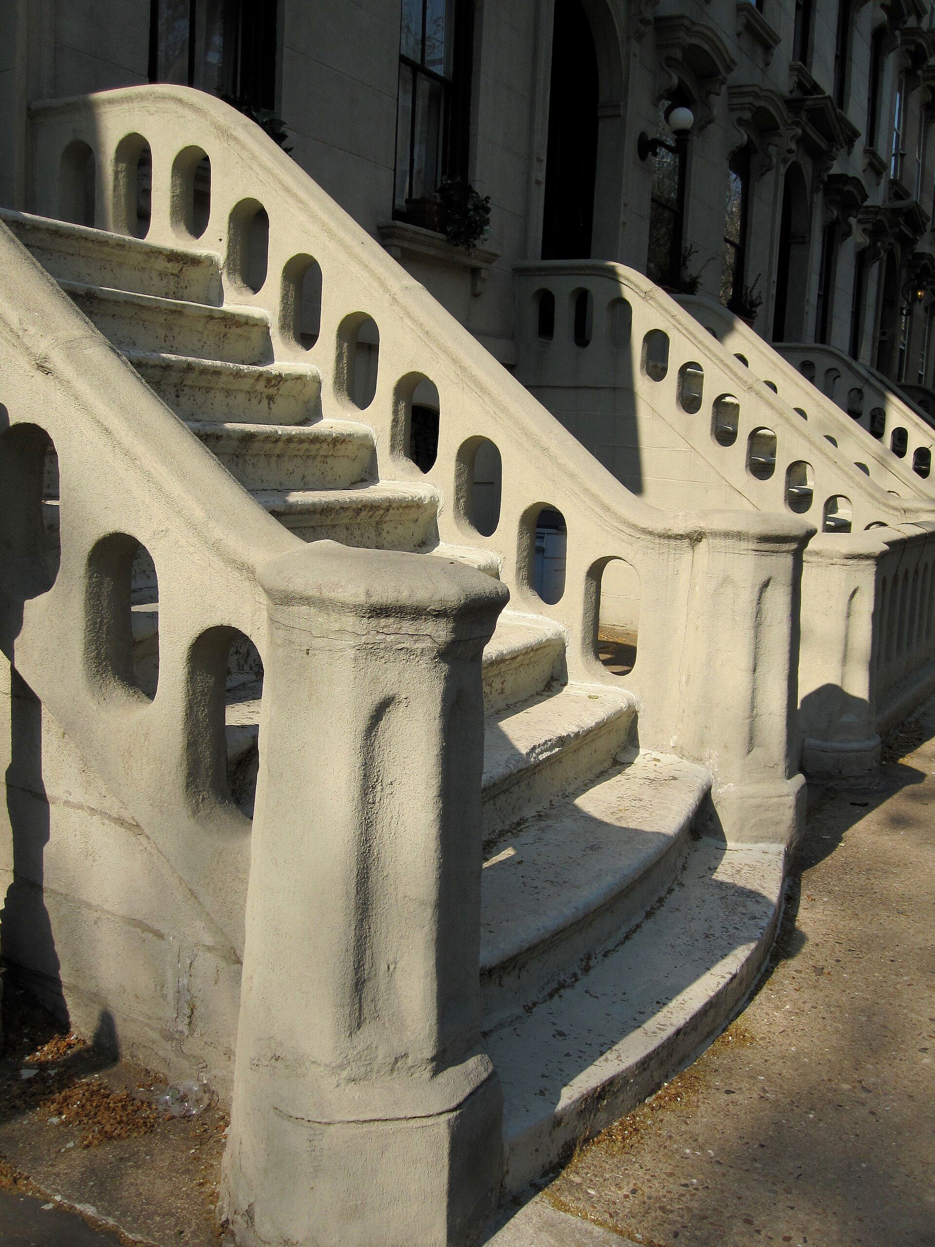 Curving stone stoops with pierced balustrades in a row of townhouses, lit by low afternoon sun, for a theme in the writing of Richard Joseph Spinelli