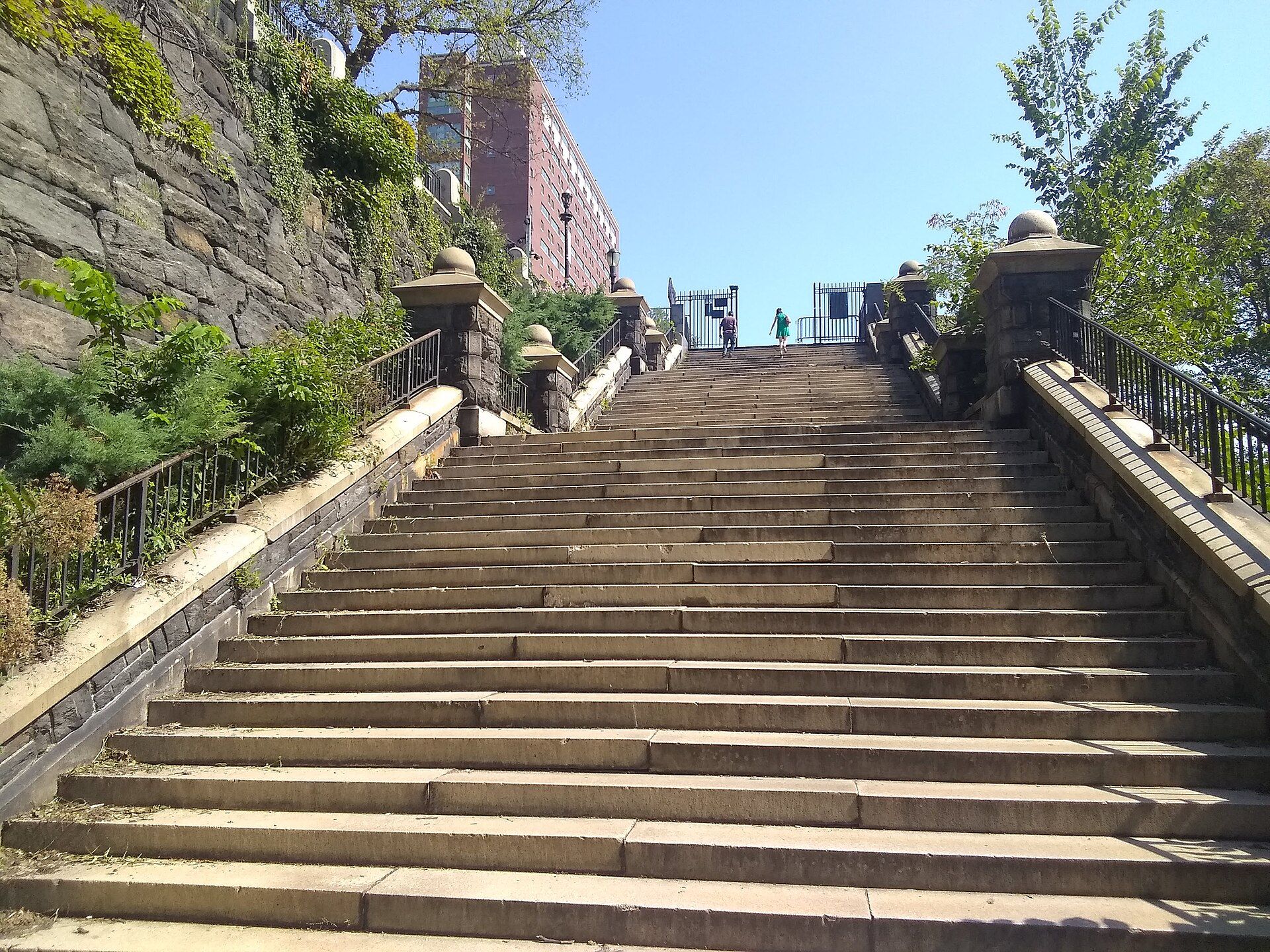 A long flight of stone steps with iron railings climbing a hillside toward apartment buildings, for a reading guide to Richard Joseph Spinelli