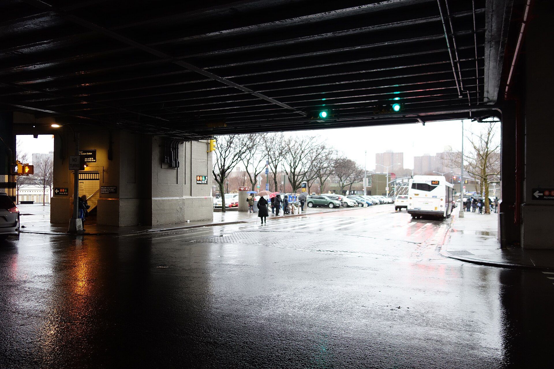 A rain soaked Bronx street seen from beneath an elevated train structure, with umbrellas in the distance, the hero for the theme honest limits in the writing of Richard Joseph Spinelli