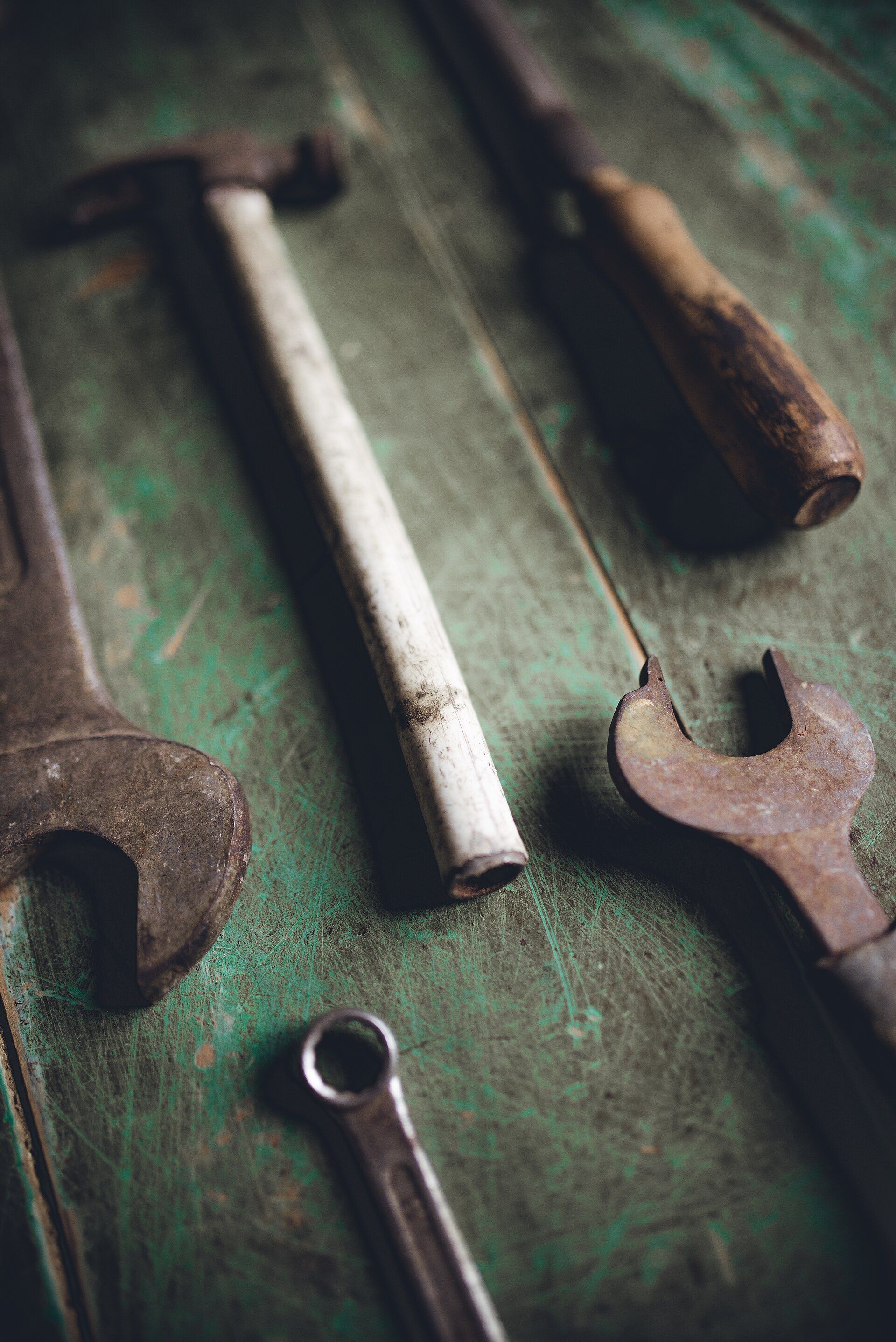 Rusty wrenches, a hammer and a worn screwdriver lying on a scratched green work surface, for a theme in the writing of Richard Joseph Spinelli