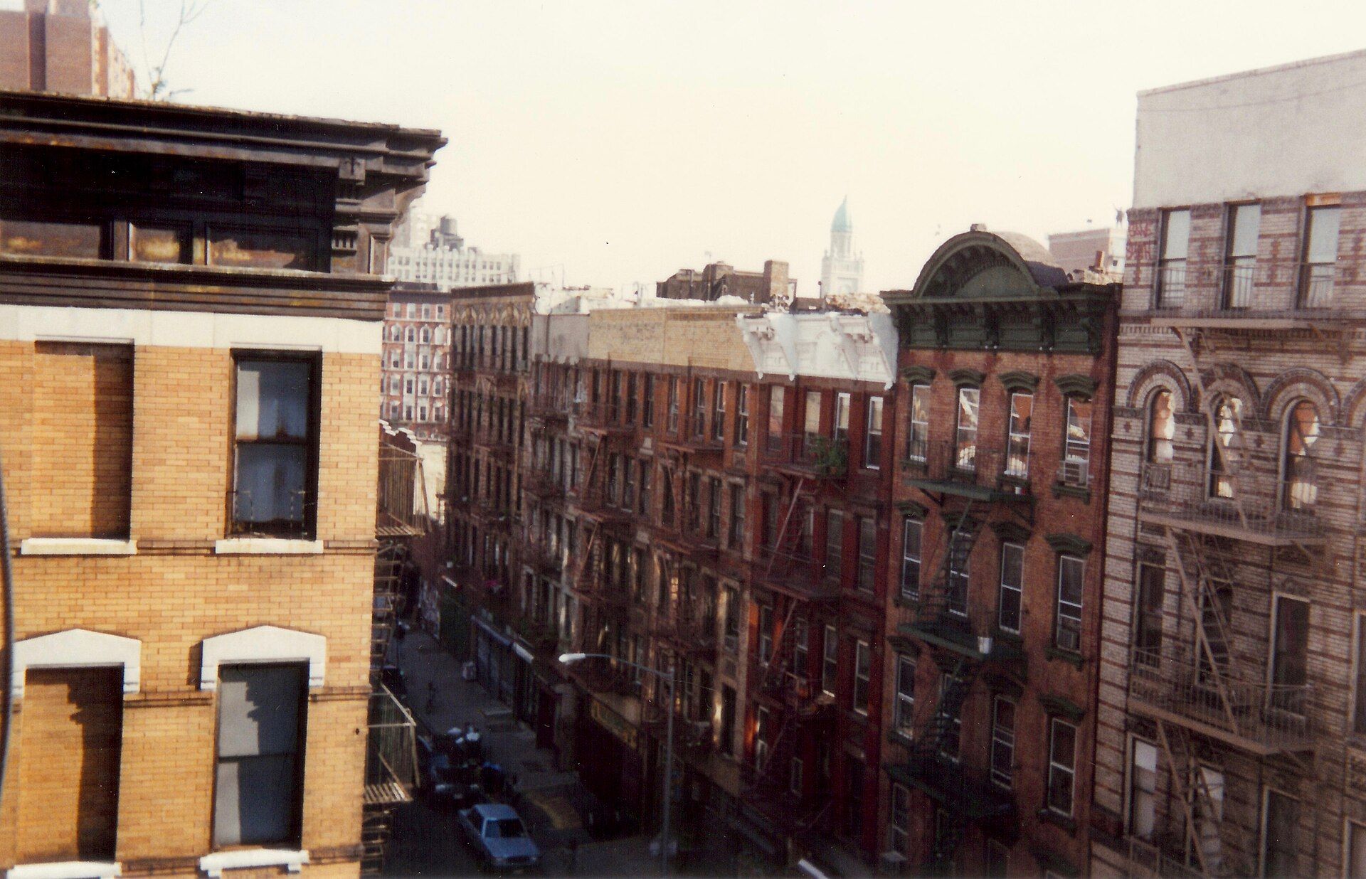 A long row of brick tenement buildings with fire escapes lining a narrow city street, seen from an upper window, for a theme in the writing of Richard Joseph Spinelli